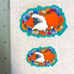 Puede incluir: Dos pegatinas con un conejillo de indias de dibujos animados rodeado de flores coloridas. El conejillo de indias es naranja y blanco con ojos negros y una nariz negra. Las flores son de varios colores, incluyendo amarillo, naranja, rojo, azul y blanco. Las pegatinas est&aacute;n sobre un fondo azul claro. El texto "@michimalillustrations" est&aacute; en la esquina inferior derecha de la pegatina m&aacute;s grande.