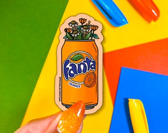 Könnte beinhalten: Ein Aufkleber mit einer Dose Fanta Orange-Limonade, aus der ein Blumenstrauß wächst. Die Dose ist orange und trägt den Schriftzug "Fanta" in weißen Buchstaben und "Orange" in schwarzen Buchstaben. Die Blumen sind weiß und gelb.