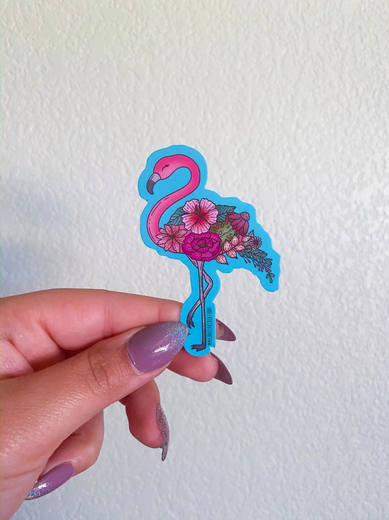 May include: A pink flamingo sticker with a blue background. The flamingo is decorated with pink, red, and green flowers. The sticker is on a white background.