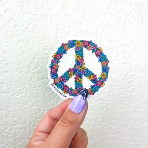 May include: A white peace sign sticker with a colorful floral design. The sticker has the text "Oh!Cara Creations" at the bottom.