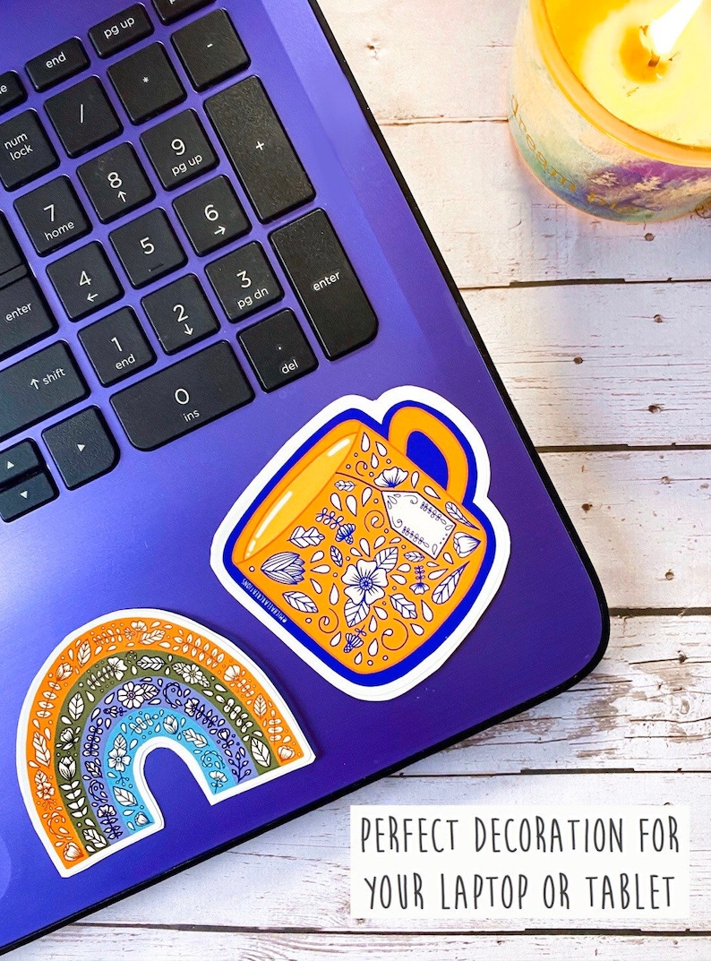 May include: Two colorful stickers on a purple laptop. One sticker is a rainbow with floral designs. The other sticker is a yellow mug with floral designs and the text "Coffee is my love language".