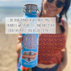 May include: A blue reusable water bottle with a stainless steel lid and multiple stickers. The stickers feature the text "Cat Mom", "She is fearless", and "Wellness".