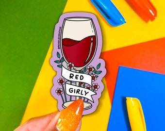 May include: A purple sticker with a wine glass filled with red wine. The glass is surrounded by pink flowers and a banner that says "Red Girly".