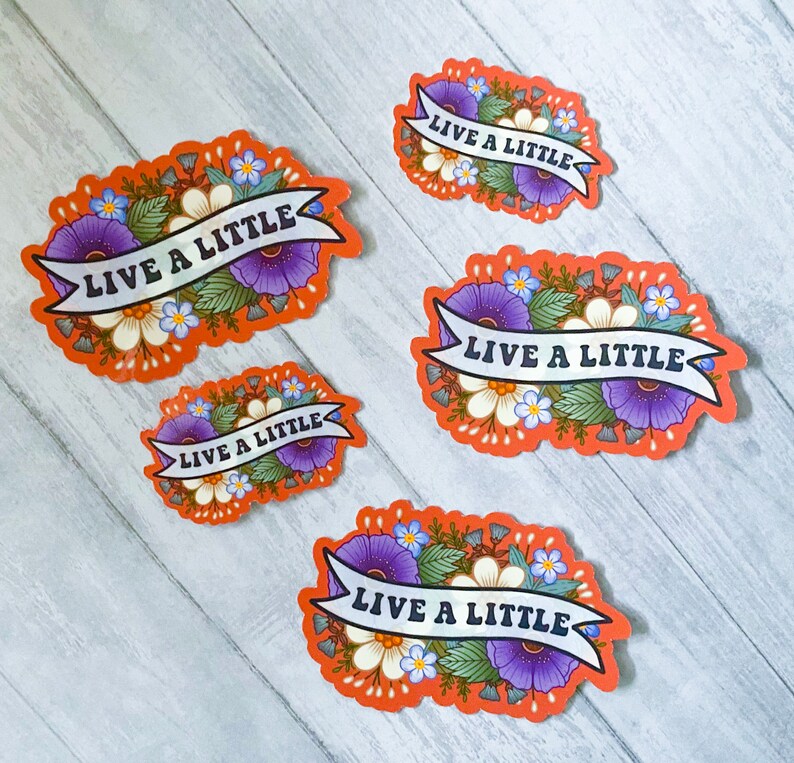May include: Four orange floral stickers with the text "Live a Little" in a white banner. The stickers have purple flowers, white flowers, and green leaves.