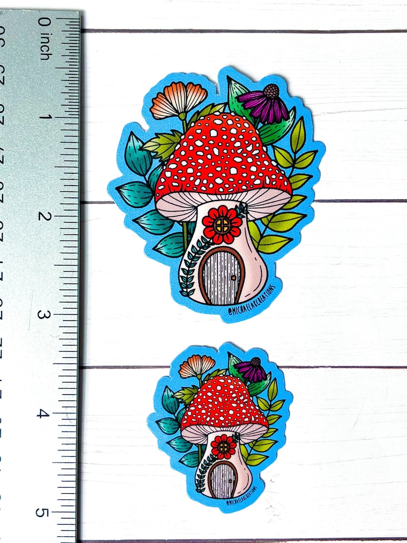 Puede incluir: Dos pegatinas de casa de seta con fondo azul. La pegatina m&aacute;s grande mide 6,5 cm de alto y la m&aacute;s peque&ntilde;a 4 cm de alto. Ambas pegatinas representan una seta roja y blanca con una puerta y una flor en la parte delantera. La seta est&aacute; rodeada de hojas verdes y flores.