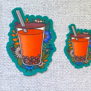 K&ouml;nnte beinhalten: Zwei Aufkleber mit einer Cartoon-Illustration eines Boba-Teas mit einem Strohhalm, umgeben von Blumen. Der gr&ouml;&szlig;ere Aufkleber ist etwa 5 cm hoch und der kleinere etwa 2,5 cm hoch.