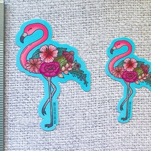 May include: Two pink flamingo stickers with floral designs. The larger sticker is 2 inches tall and features the text "@mirareafabrications". The smaller sticker is 1 inch tall and features the text "@mirareafabrications".