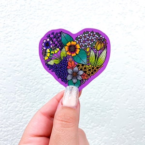 May include: A purple heart-shaped sticker with a colorful floral design. The flowers are in shades of yellow, orange, red, purple, and blue.