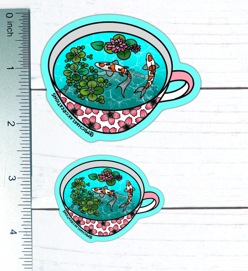 May include: A sticker of a teacup with a blue and white floral pattern. The teacup is filled with water and two orange and white koi fish. The sticker is on a white wooden background.