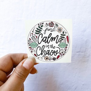 May include: A white sticker with a black circle and floral design. The text inside the circle reads "find calm in the chaos".