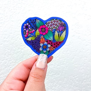 May include: A blue heart-shaped sticker with a colorful floral design. The flowers are pink, purple, white, and green. The sticker is perfect for adding a touch of whimsy to any surface.