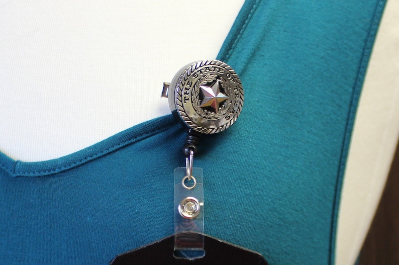 May include: Silver retractable badge holder with a round, silver charm featuring the words "The State of Texas" and a five-pointed star.
