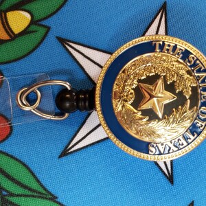 May include: A gold-colored retractable badge holder with a blue and gold seal featuring a five-pointed star and the text "THE STATE OF TEXAS".