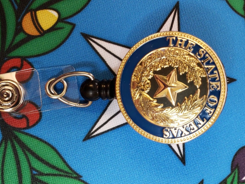 May include: A gold-colored retractable badge holder with a blue and gold seal featuring a five-pointed star and the text "THE STATE OF TEXAS".