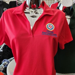 May include: Red short-sleeved polo shirt with a small embroidered logo on the left chest. The logo is a yellow circle with a blue star and a wreath of green leaves. The text "DPS TEXAS Department of Family and Protective Services" is written below the circle.