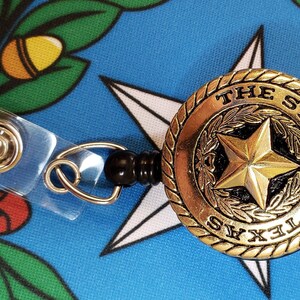 May include: A gold-colored retractable badge holder with a black plastic clip. The badge holder features a round, gold-colored emblem with the words "THE STATE OF TEXAS" and a five-pointed star.