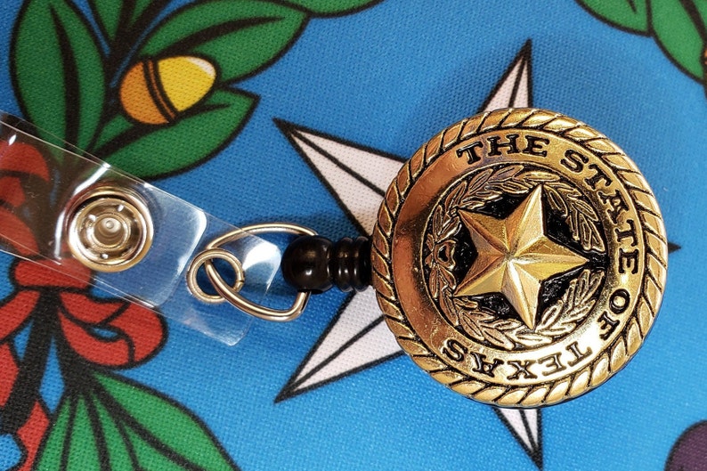 May include: A gold-colored retractable badge holder with a black plastic clip. The badge holder features a round, gold-colored emblem with the words "THE STATE OF TEXAS" and a five-pointed star.