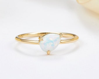 Puede incluir: Un delicado anillo de oro con una piedra de ópalo en forma de pera. El anillo está sobre un fondo blanco.