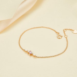 May include: A delicate gold chain bracelet with a pink and white gemstone cluster. The bracelet has a lobster clasp closure.