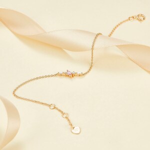 May include: A delicate gold chain bracelet with a pink and white gemstone cluster. The bracelet has a heart-shaped charm with the word "Love" inscribed on it.