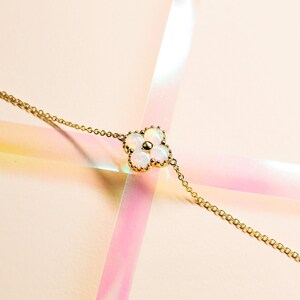 May include: A delicate gold chain bracelet with a five-petal flower charm. The flower is made of white opal stones set in gold.