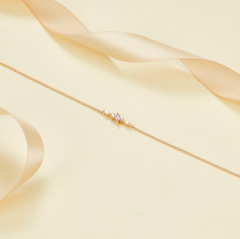 May include: A delicate gold chain bracelet with a small pink gemstone and clear stones in a starburst design.