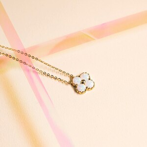 May include: A gold chain necklace with a white opal flower pendant. The flower has five petals and a small gold center.