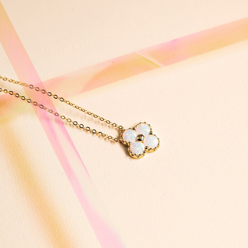 May include: A gold chain necklace with a white opal flower pendant. The flower has five petals and a small gold center.