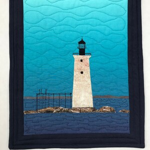 May include: A white lighthouse with a black roof and a black lantern on top stands on a rocky island in a blue ocean. The sky is a gradient of blue and turquoise with white clouds. The image is framed with a dark blue border.