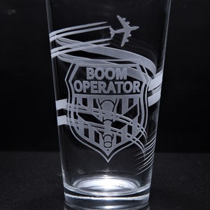 May include: A clear glass with an etched design of an airplane, a shield with the words "BOOM OPERATOR" and a microphone inside the shield.