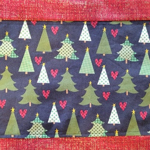 May include: A red and gold fabric table runner with a repeating pattern of green Christmas trees and red hearts on a dark blue background.