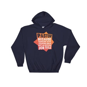 May include: Navy blue hooded sweatshirt with a graphic design that reads "PASTOR BECAUSE HARDCORE DEVIL STOMPING NINJA ISN'T AN OFFICIAL JOB TITLE". The graphic is in orange and yellow.