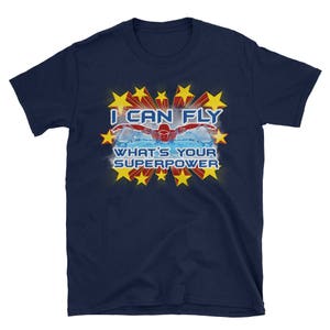 Peut inclure: T-shirt bleu marine avec un graphique de nageur rouge, blanc et bleu et le texte "Je peux voler. Quel est ton super pouvoir ?"