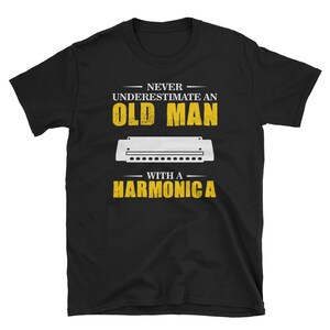 May include: Black t-shirt with yellow text that reads "Never underestimate an old man with a harmonica". A white harmonica is pictured below the text.
