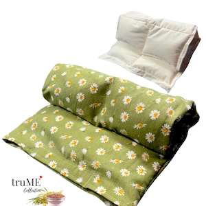 May include: Two aromatherapy eye pillows and a neck wrap. The neck wrap is green with a white daisy pattern. The eye pillow is a solid off-white color. The truME Collection logo is in the bottom left corner.