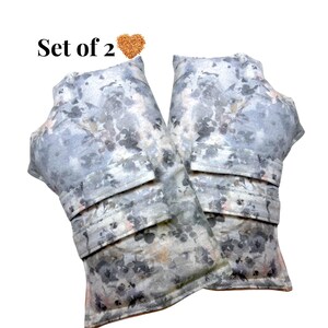 May include: Set of 2 gray and white floral patterned heat packs. The heat packs have a rectangular shape with a curved top and a folded section. The text "Set of 2" is above the heat packs.