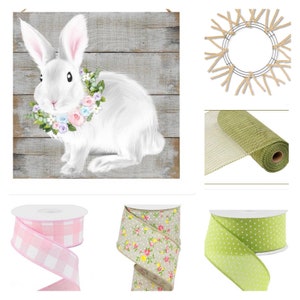 May include: A white bunny with a floral wreath around its neck sits on a weathered wood background. The bunny is surrounded by a wreath, green mesh, pink and white gingham ribbon, floral ribbon, and green polka dot ribbon.