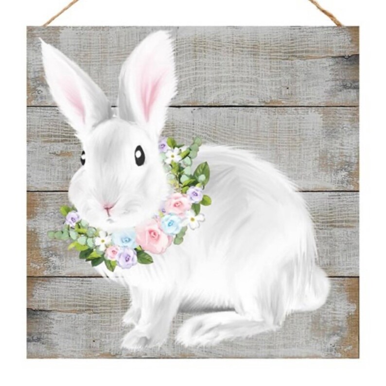 May include: A white rabbit with a pink, blue, and white flower crown sits on a gray wooden background.