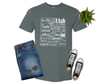 Może przedstawiać: Szary t-shirt w ciemnym odcieniu z białym obrysem stanu Utah i nazwami wszystkich hrabstw w stanie. Tekst brzmi: Box Elder, Cache, Tooele, Juab, Millard, Beaver, Iron, Washington, Summit, Daggett, Duchesne, Uintah, Emery, Grand, Wayne, Garfield, Kane, San Juan, Utah.