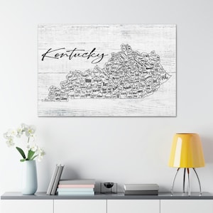 Può includere: Una mappa in bianco e nero del Kentucky con i nomi di tutte le contee dello stato. La mappa è su uno sfondo di legno bianco. La parola "Kentucky" è scritta in corsivo nero nella parte superiore della mappa.