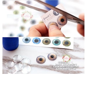 May include: A sheet of colorful glass eyes for doll making. The eyes are on a white sheet with the text "c forest II IPS PATTERN 1". There are clear glass eyes and a pair of glass eyes with a purple, blue, and brown iris.