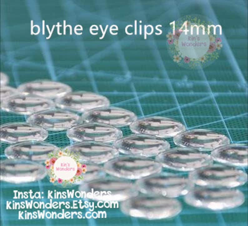 May include: A close-up of a group of clear plastic eye clips for Blythe dolls. The clips are 14mm in diameter and are arranged in rows on a blue cutting mat. The text "blythe eye clips 14mm" is visible at the top of the image.