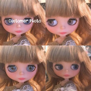 May include: A close-up of a doll with long, wavy, light brown hair. The doll has blue eyes and is wearing a brown and white dress. The doll's face is painted with a delicate blush and a light pink lip color. The doll's eyes are large and expressive, and the doll's overall appearance is sweet and innocent.