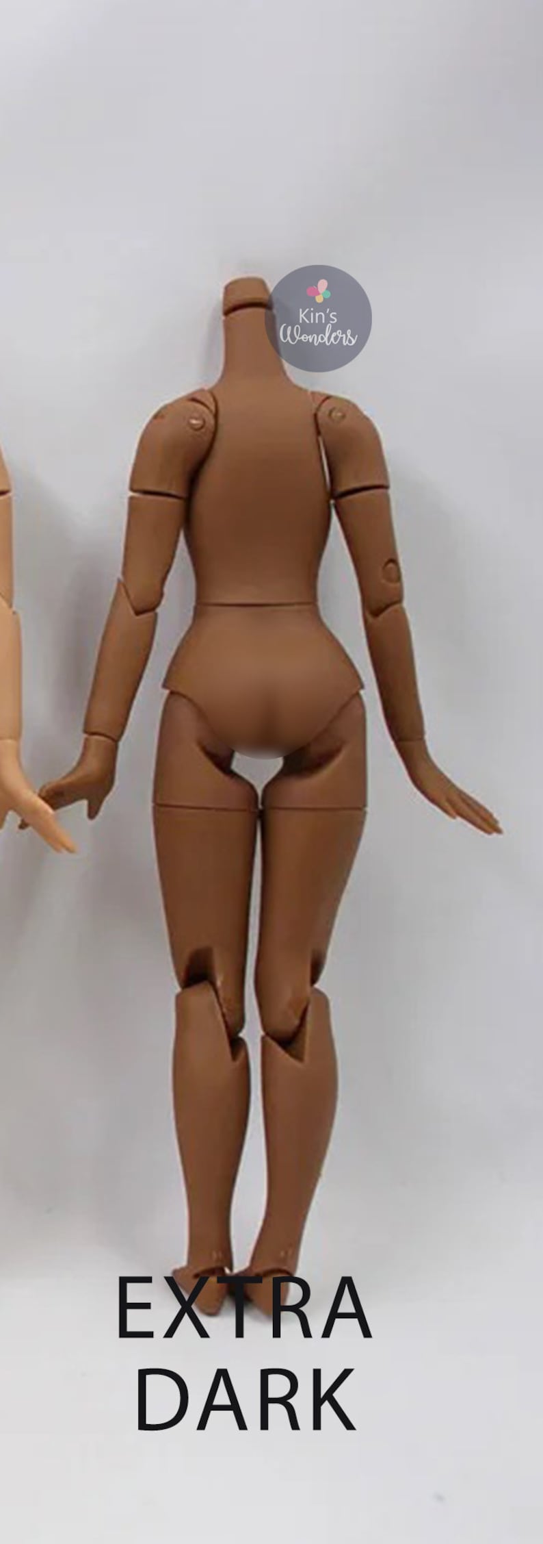 May include: A brown articulated doll body with the text "EXTRA DARK" printed below. The doll is posed with its arms outstretched and legs bent at the knees.