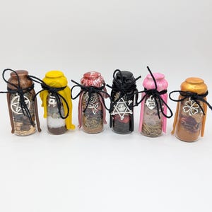 May include: Six small glass bottles filled with various dried herbs, crystals, and powders. Each bottle has a colored wax seal, a black string tie, and a silver-toned metal charm, including a pentagram, rose, eye, and a heart reading Made with Love.