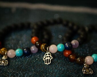 May include: Two beaded bracelets with colourful stones and silver charms. One charm is a hamsa hand and the other is a small animal figure.