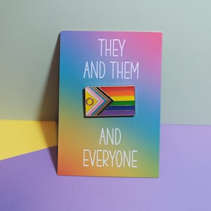Può includere: Uno spillo color arcobaleno con il testo "They and Them and Everyone" su una carta con uno sfondo sfumato arcobaleno.