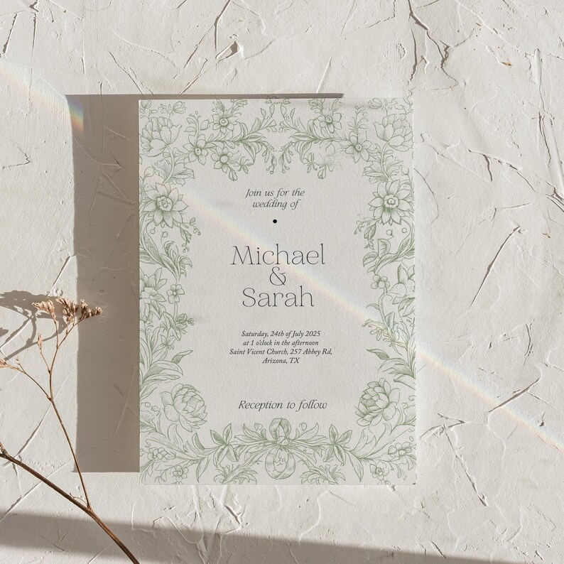 Op de afbeelding: Een trouwuitnodiging met een lichtgroene bloemenrand. De tekst luidt "join us for the wedding of Michael & Sarah" met datum, tijd en locatie eronder. De uitnodiging staat op een witte, getextureerde achtergrond.