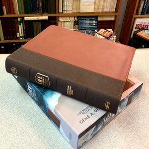 May include: A brown leather-bound Bible with the title "Life Potential" on the spine. The Bible is sitting on a box with a blue and white wave design and the text "1500 Principles to Live By Gene A. Ge. Holman Life".