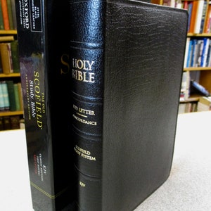 May include: Black leather-bound Scofield Study Bible with gold lettering. The title "The Old Scofield Study Bible" is on the spine. The Bible is closed and sitting on a table.